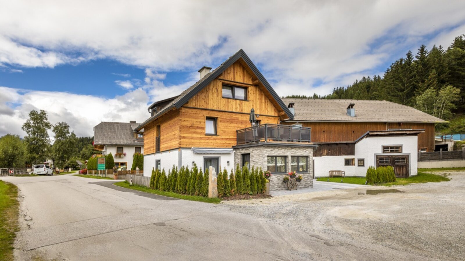 Außenansicht des Bauernhofs mit Holzfassade, Balkon und Schotterparkplatz.