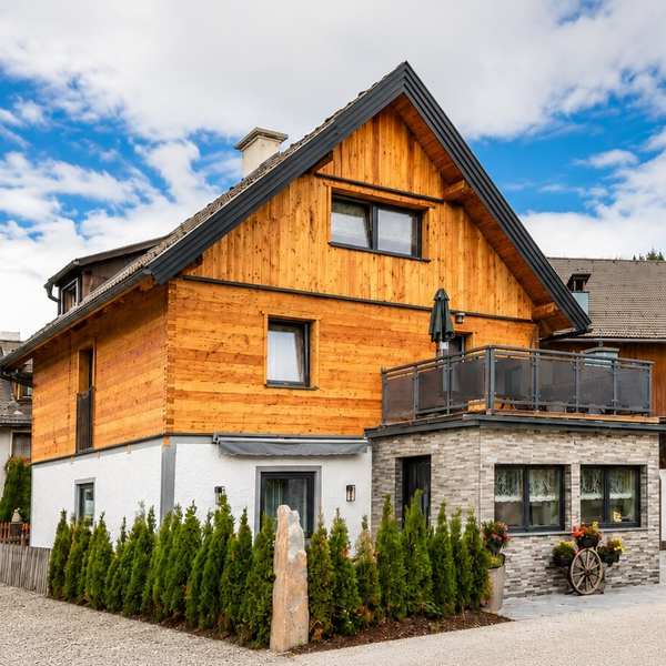 Die charmante Außenansicht des Bauernhofs mit rustikaler Holzfassade, Balkon und gepflegten Hecken.