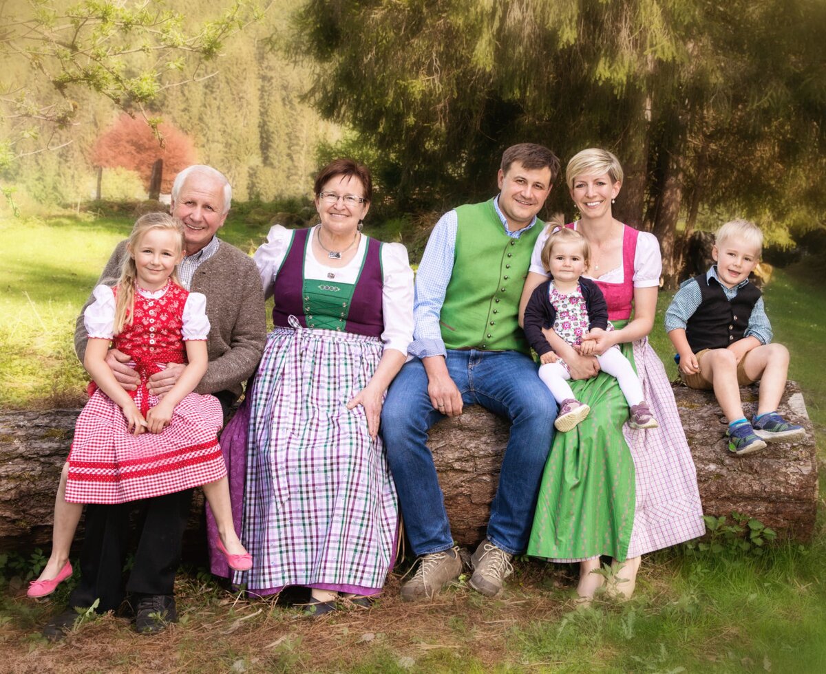 Die Gastgeberfamilie des Bauernhofs, bestehend aus drei Generationen in traditioneller Kleidung, heißt Sie herzlich willkommen.