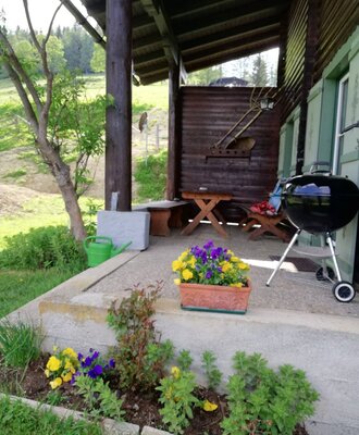 Überdachter Außenbereich des Hofes mit Holzsitzgruppe und Grill.
