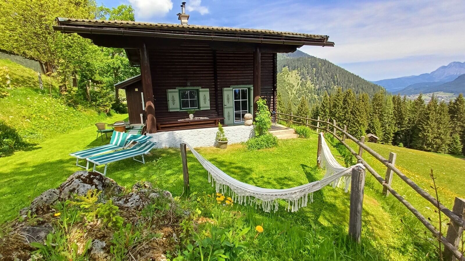 Der Hof mit Rasenfläche, Liegestühlen, Hängematte und einer Berglandschaft im Hintergrund.