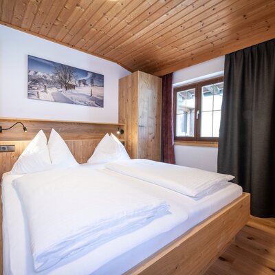 Doppelzimmer im Appartement mit Holzbett, integrierten Leselampen, Holzschrank, Holzdecke und Fenster.