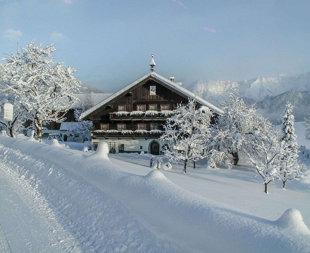 Der verschneite Bauernhof in einer malerischen Winterlandschaft mit Blick auf die umliegenden Berge.