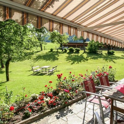 Die einladende Terrasse des Bauernhofs mit schattenspendender Markise und Blick auf die weitläufige, grüne Wiese.