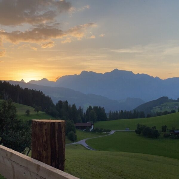 Blick auf den Sonnenuntergang über einer Berglandschaft mit grünen Feldern und Häusern vom Bed and Breakfast aus.