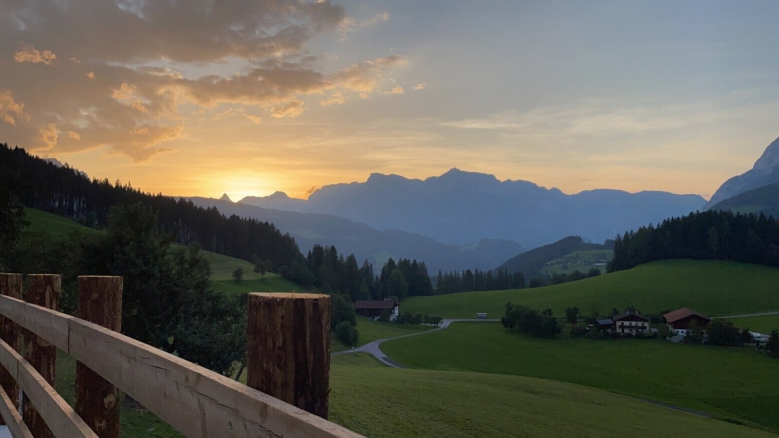 Blick auf den Sonnenuntergang über einer Berglandschaft mit grünen Feldern und Häusern vom Bed and Breakfast aus.