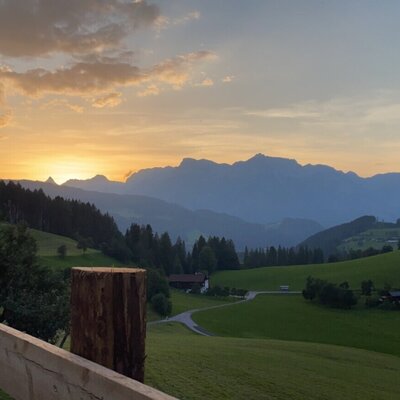 Blick auf den Sonnenuntergang über einer Berglandschaft mit grünen Feldern und Häusern vom Bed and Breakfast aus.