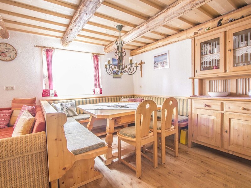 Der Essbereich des Hofs mit Eckbank, Holztisch, Stühlen und einem Geschirrschrank unter einer Holzbalkendecke.