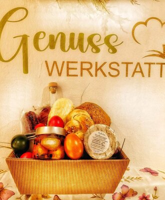 Ein Korb mit frischen Backwaren, Käse und Eiern, präsentiert unter dem Schild 'Genuss Werkstatt' im Bed and Breakfast.