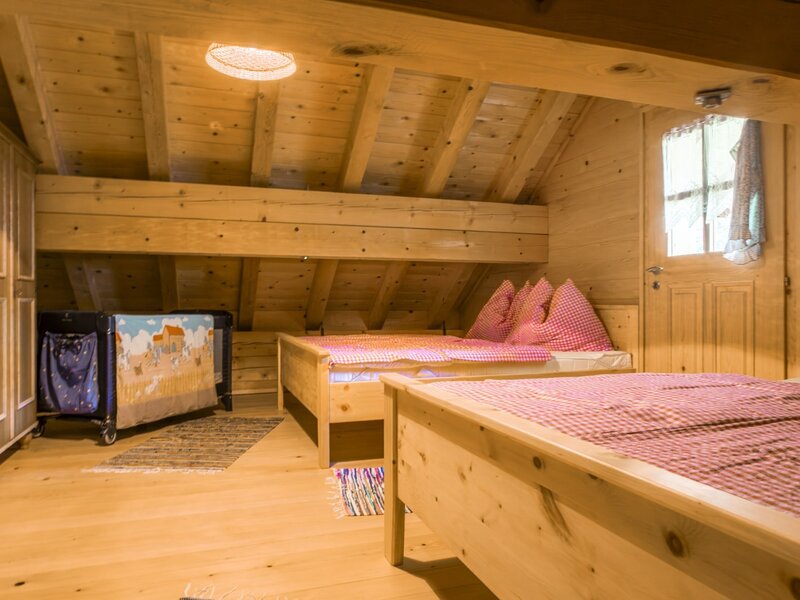Ein gemütliches Schlafzimmer der Almhütte mit traditionellen Holzmöbeln, karierter Bettwäsche und einem praktischen Gitterbett.
