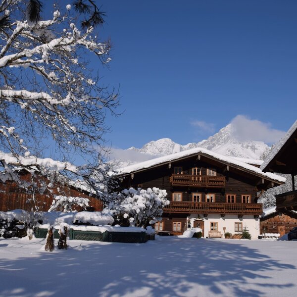 Die Außenansicht des Bauernhofs im Winter, mit schneebedeckter Landschaft und Bergblick.