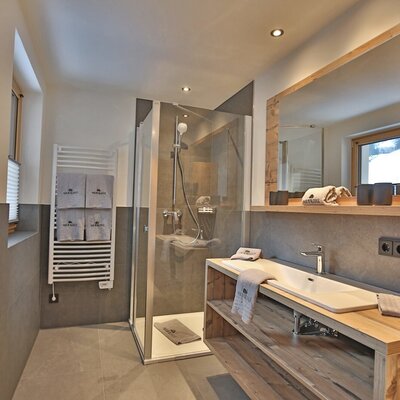 Badezimmer im Bauernhof mit Duschkabine, Waschbecken auf Holzunterschrank, großem Spiegel, Haartrockner und Handtuchheizkörper.