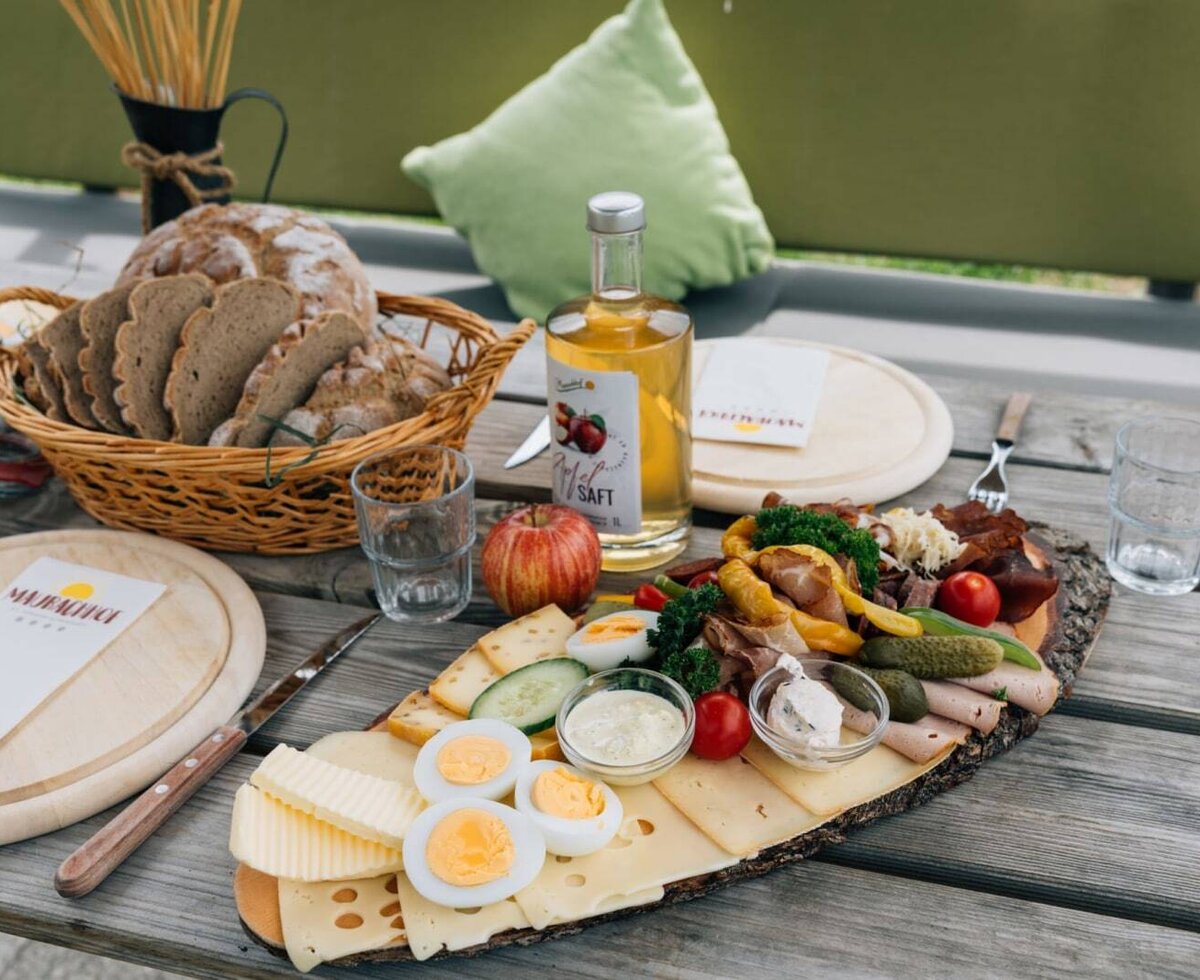 Eine reichhaltige Jausenplatte auf dem Bauernhof mit frischem Brot, Käse, Aufschnitt und Apfelsaft auf einem rustikalen Holztisch.