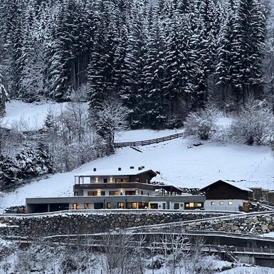 Außenansicht des Kitzlochklammblick-Hofs in Taxenbach, eingebettet in eine schneebedeckte Landschaft mit bewaldeten Hügeln.
