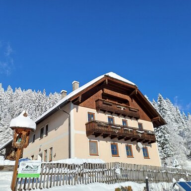 Außenansicht des Bauernhofs Krametergut in der verschneiten Winterlandschaft unter blauem Himmel.
