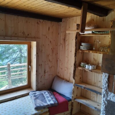 Sitzbank am Fenster mit Blick auf die bewaldete Landschaft, Holzregale mit Geschirr und ein gemauerter Kamin im Hof.