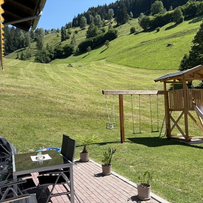 Die einladende Terrasse mit einem schattigen Sitzbereich, einem Kinderspielplatz und Blick auf die Berghänge.
