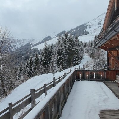 Blick von der Alm auf die verschneite Berglandschaft mit einer Holzterrasse.