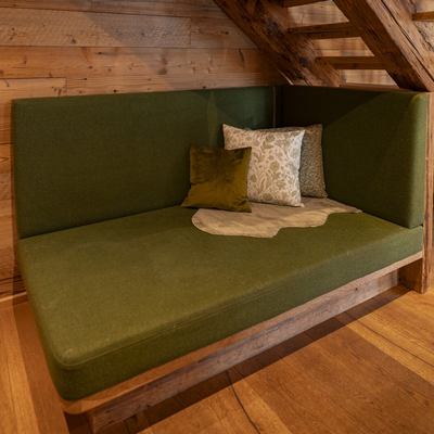 Grüne Eckbank mit Kissen und Holztreppe in der Alm.