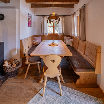 Essbereich in der Alm mit Holzesstisch, Eckbank, Stühlen und einem brennenden Kaminofen.