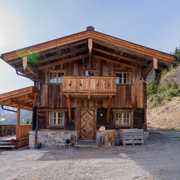 Außenansicht der Alm mit Holzbalkon, Steinfundament und überdachter Terrasse.