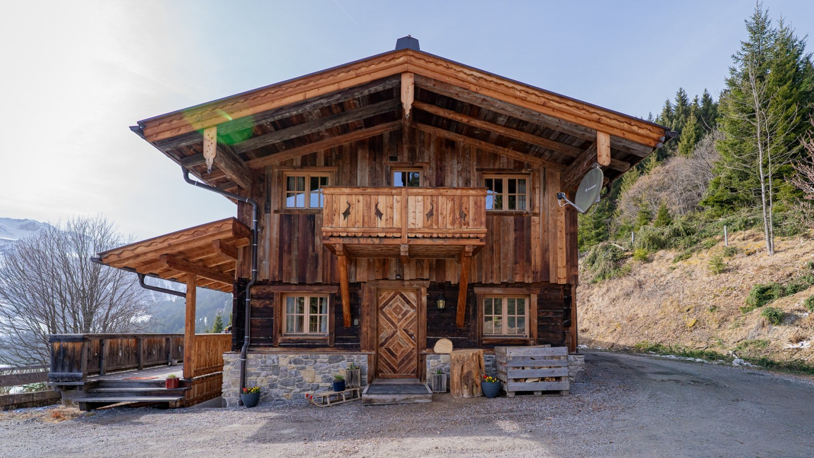 Außenansicht der Alm mit Holzbalkon, Steinfundament und überdachter Terrasse.