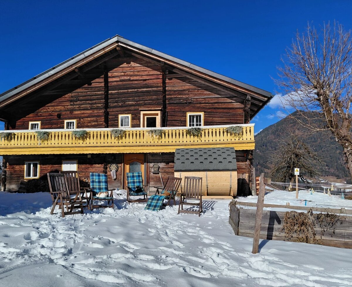 Das charmante Bed and Breakfast mit einer sonnigen, verschneiten Terrasse, gemütlichen Liegestühlen und einer Fasssauna vor einer malerischen Bergkulisse.