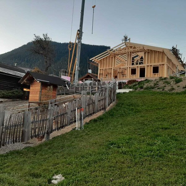Außenansicht des im Bau befindlichen Bed and Breakfast mit Holzrahmen, Kran und einem eingezäunten Bereich mit kleinem Holzschuppen.