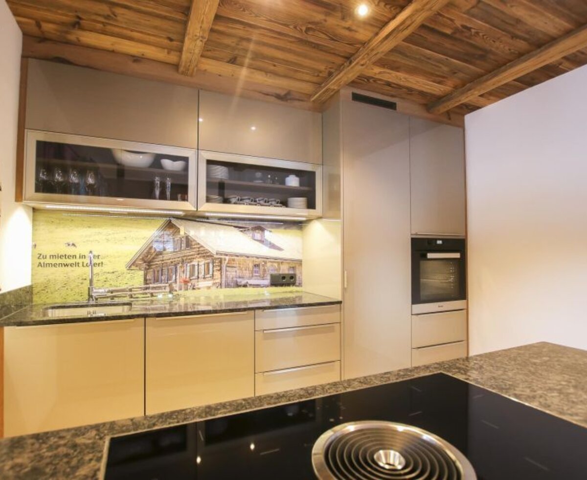 Moderne Küche im Bed and Breakfast mit Induktionskochfeld, Backofen und einer Spüle mit Almhütten-Rückwand unter einer Holzdecke.