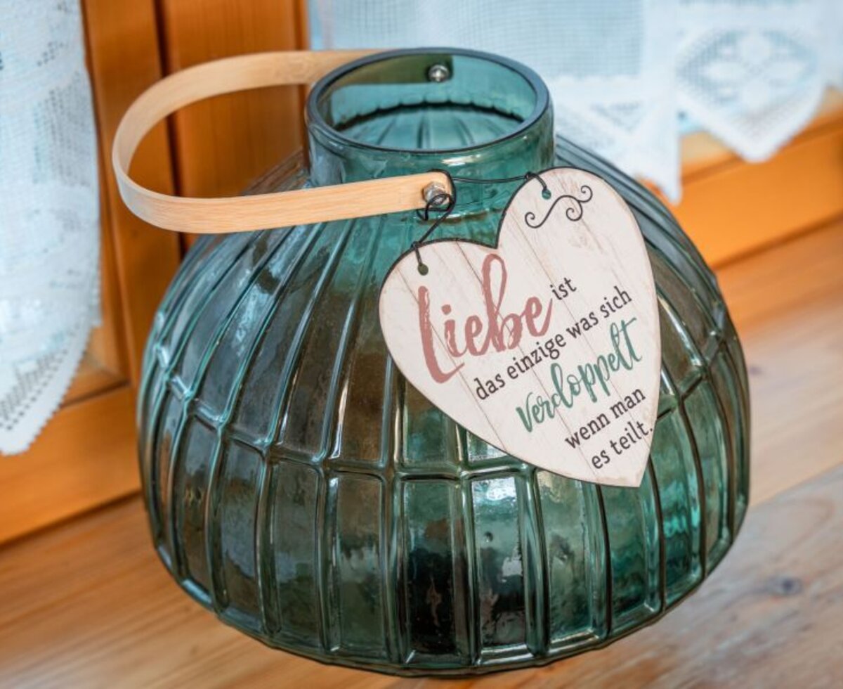 Dekorative Glaslaterne mit Herzanhänger und der Aufschrift 'Liebe ist das einzige was sich verdoppelt wenn man es teilt' im Bed and Breakfast.