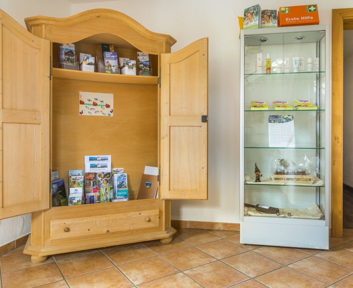 Ein Informationsschrank mit Ausflugsbroschüren und eine Vitrine mit Erste-Hilfe-Artikeln und weiteren Produkten für Gäste im Bauernhof.