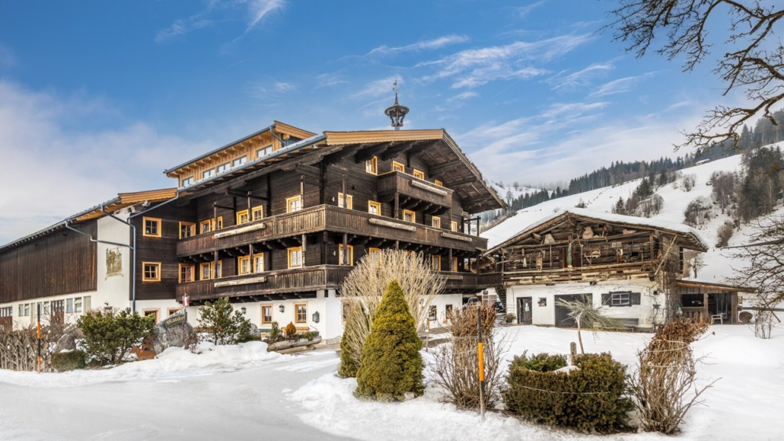 Der Bauernhof im Winter, mit dem Hauptgebäude der Apartments, einem traditionellen Nebengebäude und schneebedeckten Hängen im Hintergrund.