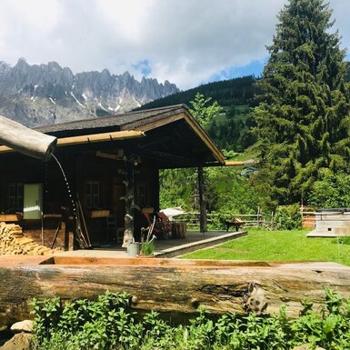 Der Hof mit überdachter Terrasse, traditionellem Holzbrunnen und Blick auf die umliegenden Berge.