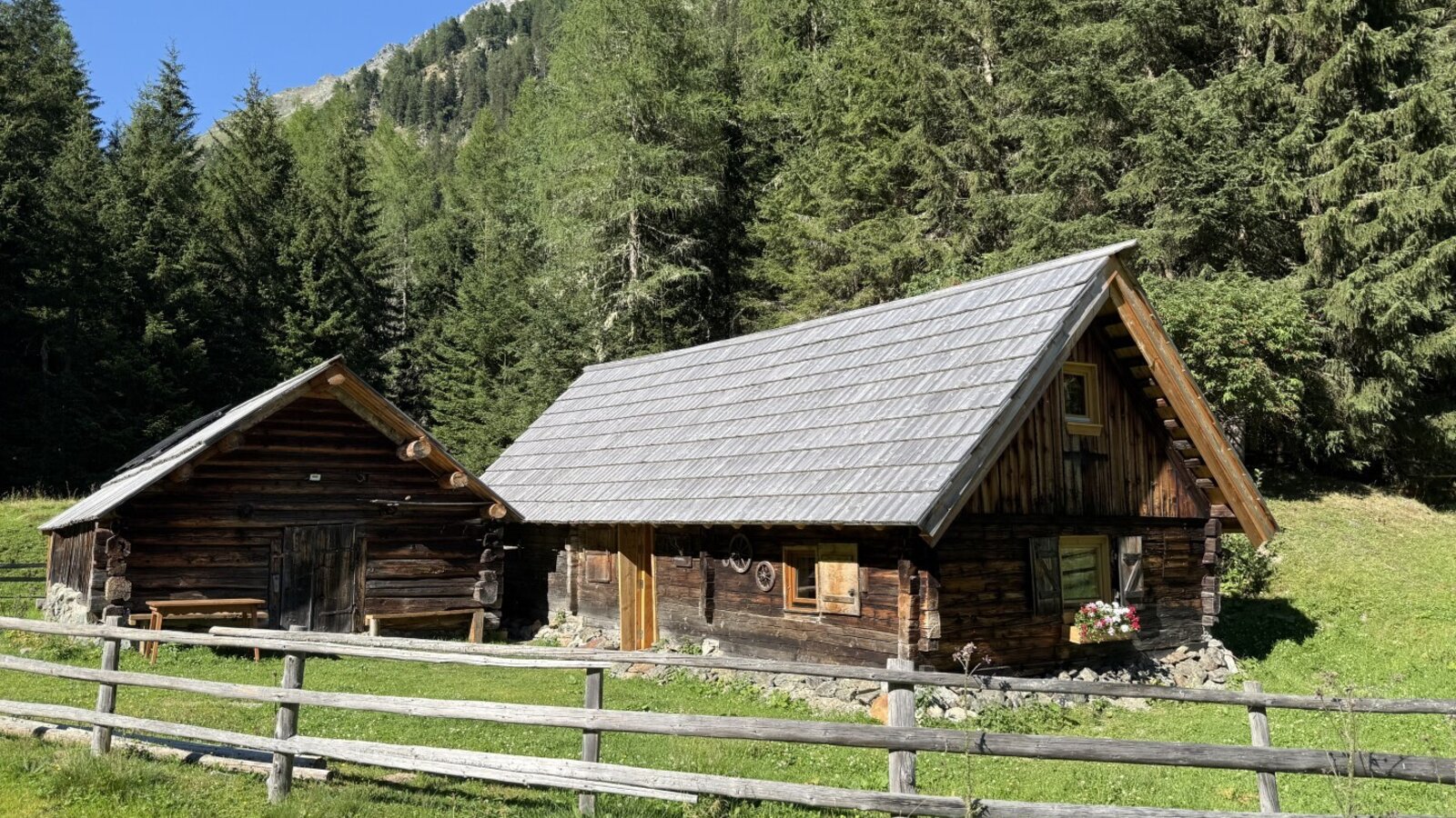 Die urigen Holzhütten des Bed and Breakfasts, eingebettet in eine saftig grüne Wiese vor einer waldreichen Bergkulisse.