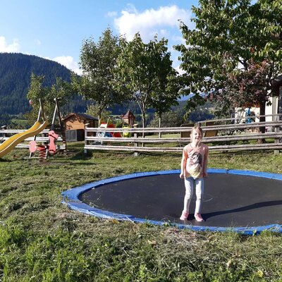 Der Spielplatz auf dem Bauernhof bietet ein Trampolin, eine Rutsche und eine Federwippe mit Bergblick.