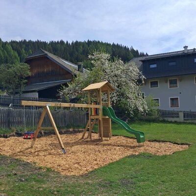 Der Spielplatz am Bauernhof mit Schaukel, Rutsche und Fallschutz aus Holzhackschnitzeln.