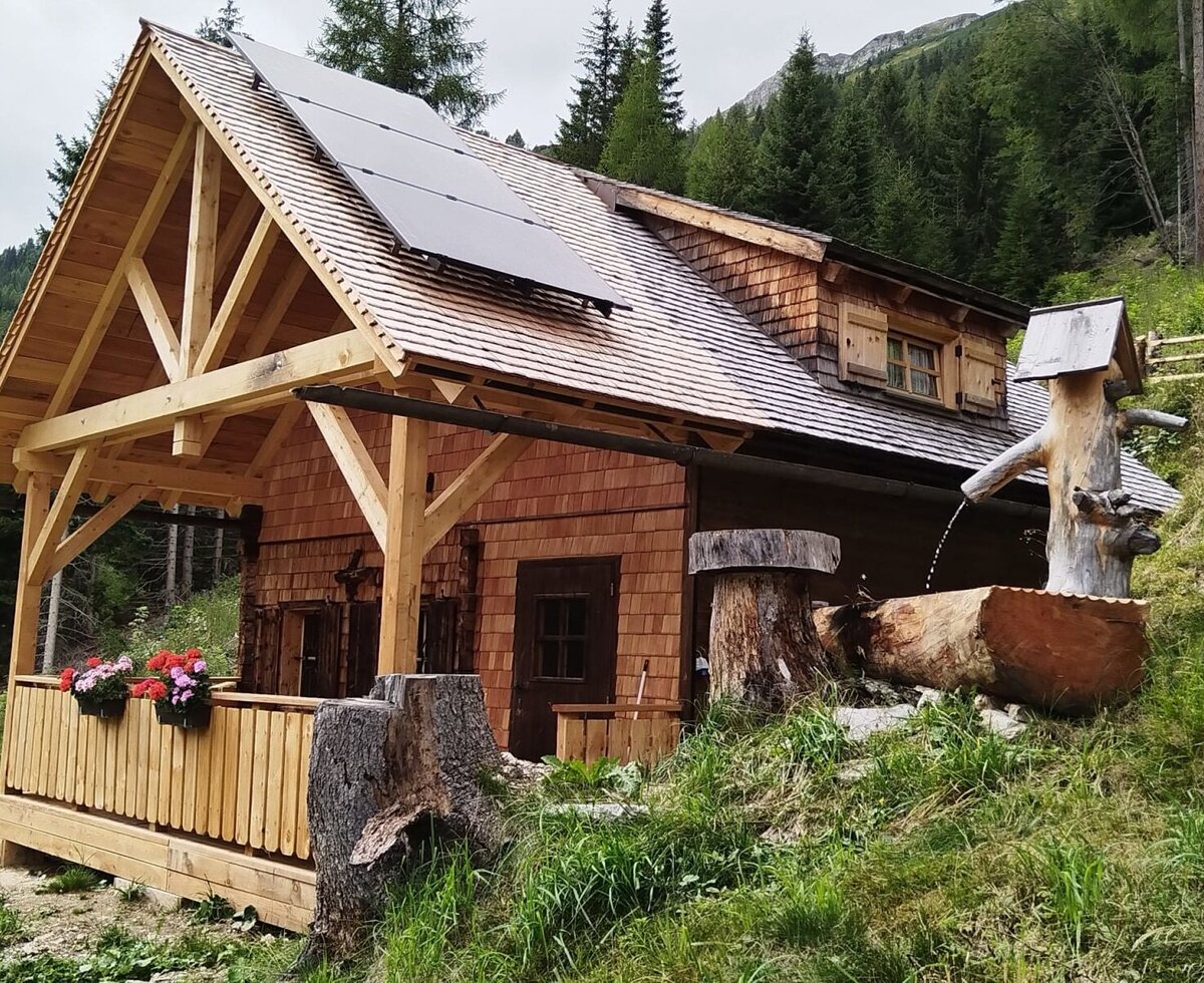 Der Hof von außen, ausgestattet mit einer überdachten Terrasse, Solarpanelen auf dem Dach und einem Holzbrunnen.