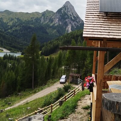 Blick vom Hof auf den Schlierersee und die Berglandschaft mit Solarmodulen auf dem Dach.