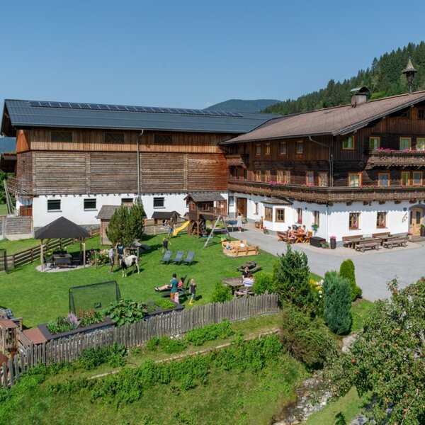 Außenansicht des Bauernhofs mit großem Garten, Kinderspielplatz, Trampolin, überdachtem Sitzbereich und Tiergehegen.