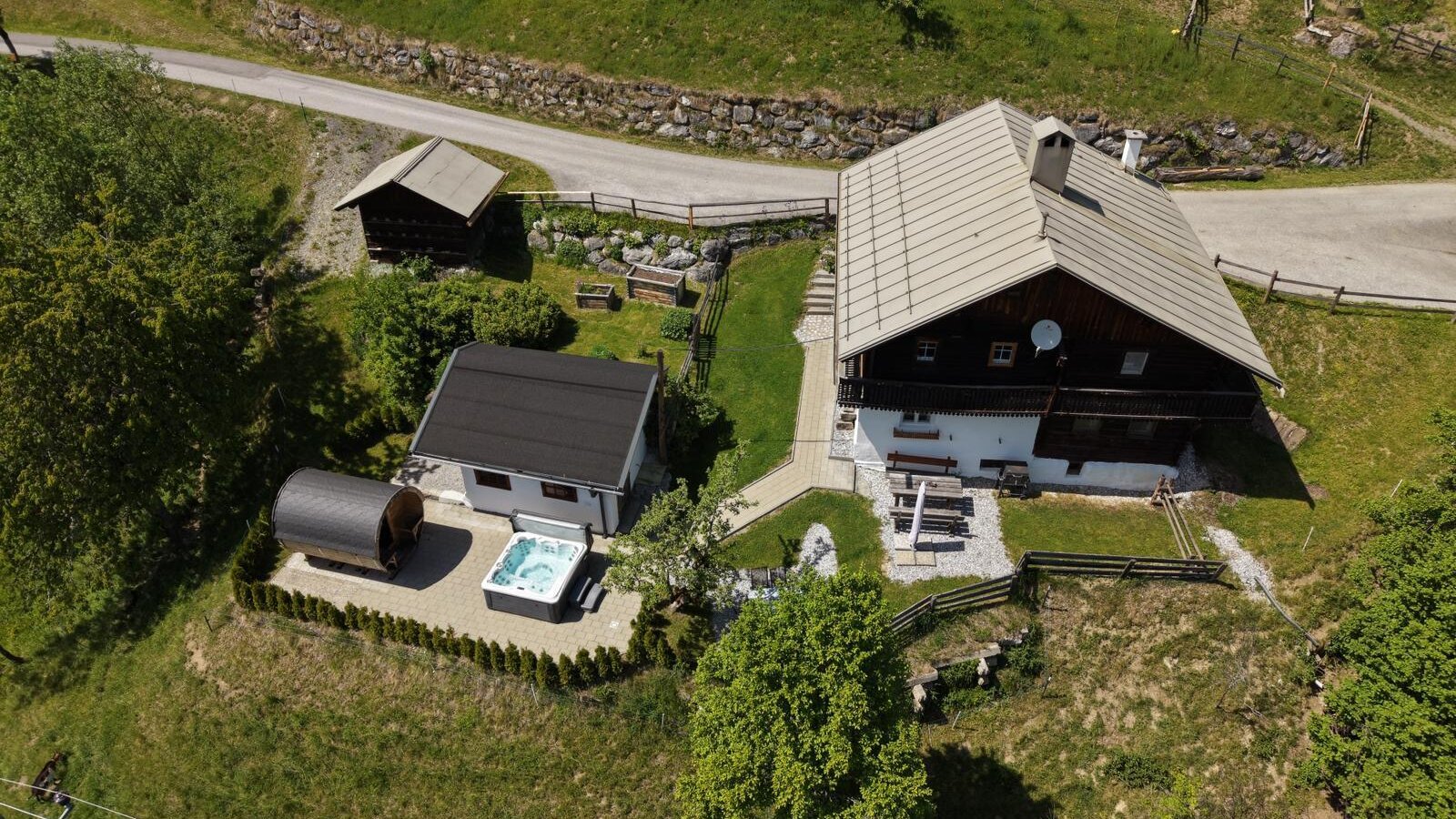 Vogelperspektive auf die idyllische Alm mit einer einladenden Außensauna und einem modernen Whirlpool im gepflegten Gartenbereich.