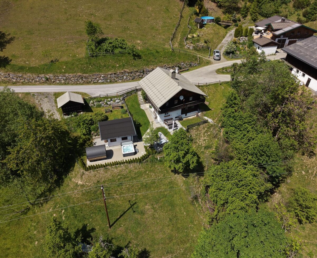 Eine idyllische Alm aus der Vogelperspektive, umgeben von grünen Wiesen und mit einem privaten Außenbereich samt Whirlpool.