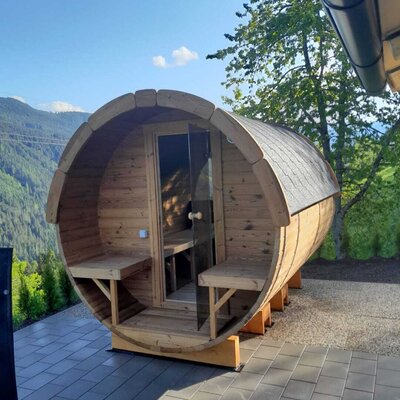 Eine einladende Fasssauna auf der Terrasse der Alm mit malerischem Blick auf die umliegenden Berge.
