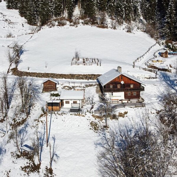 Die gemütliche Alm liegt idyllisch inmitten einer verschneiten, sonnigen Berglandschaft.