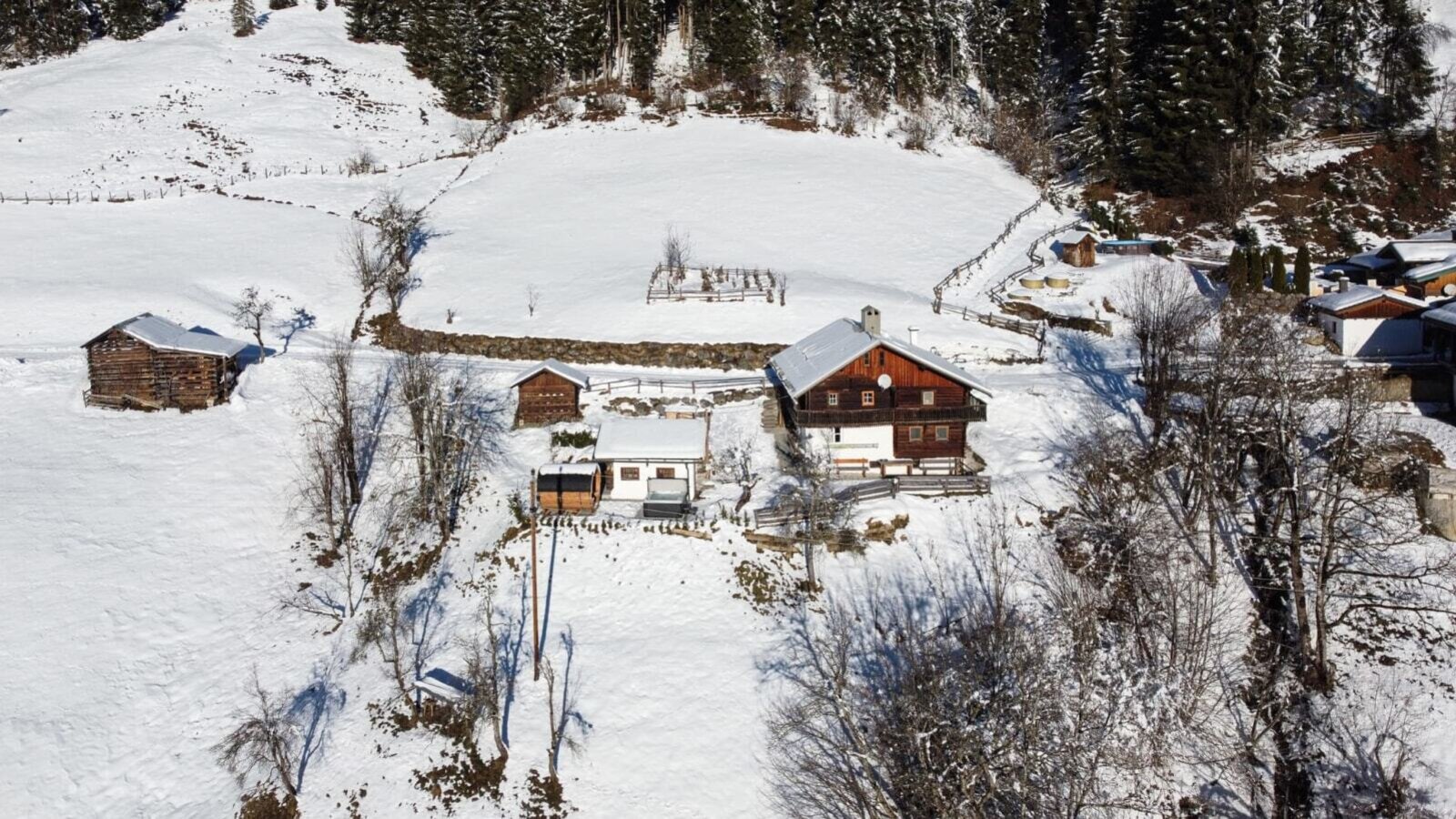Die gemütliche Alm liegt idyllisch inmitten einer verschneiten, sonnigen Berglandschaft.