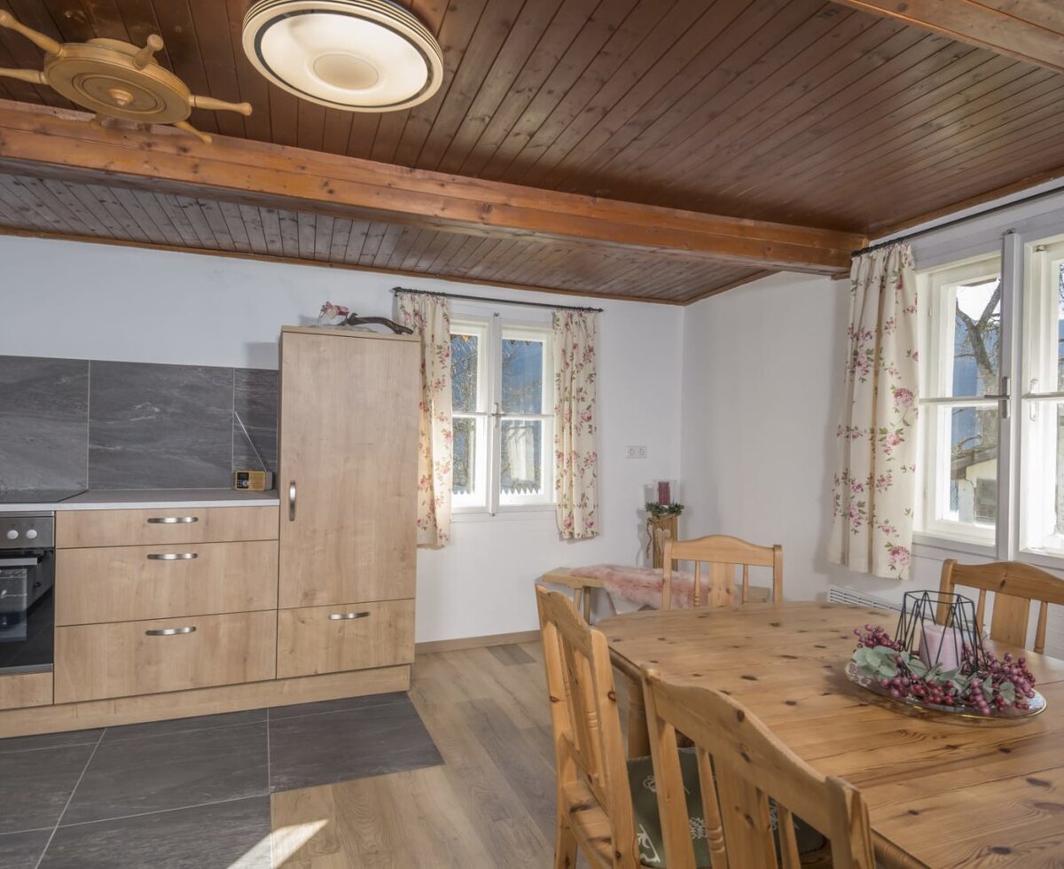 Eine gemütliche Wohnküche in der Alm mit einer hellen Holz-Essecke, rustikaler Holzdecke und einer modernen Küchenzeile.