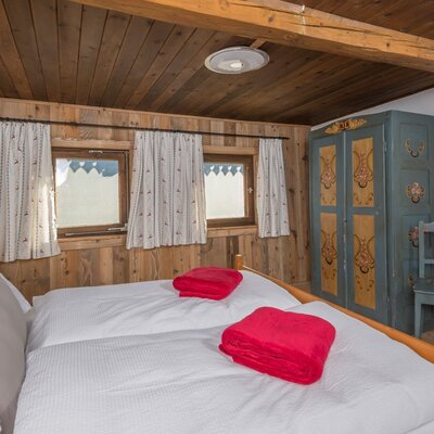 Ein gemütliches Schlafzimmer in der Alm mit rustikalen Holzwänden, einem Doppelbett und bemalten Bauernmöbeln.