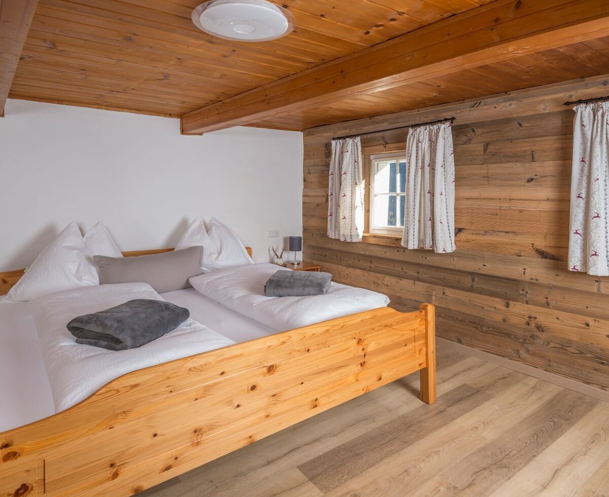 Ein gemütliches Schlafzimmer auf der Alm mit einem rustikalen Doppelbett aus Holz und urigen Holzwänden.