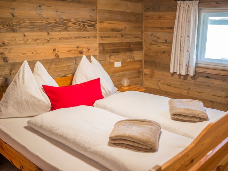 Ein gemütliches Schlafzimmer in der Alm mit rustikalen Holzwänden, einem komfortablen Doppelbett und weicher Bettwäsche.