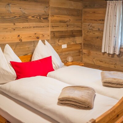 Ein gemütliches Schlafzimmer in der Alm mit rustikalen Holzwänden, einem komfortablen Doppelbett und weicher Bettwäsche.