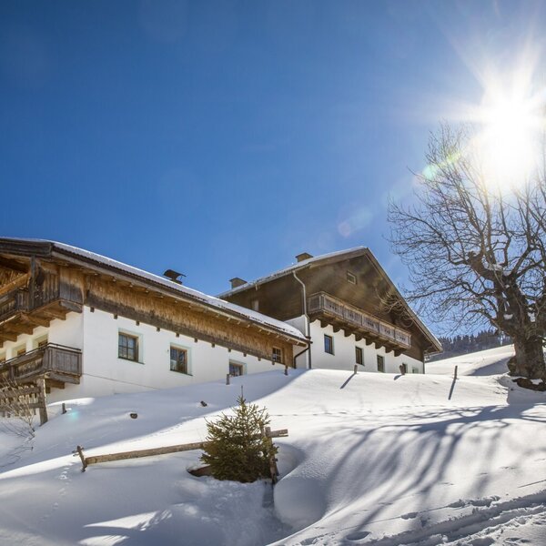 Der Bauernhof im Winter, mit Schnee und Balkonen, unter einem sonnigen Himmel.